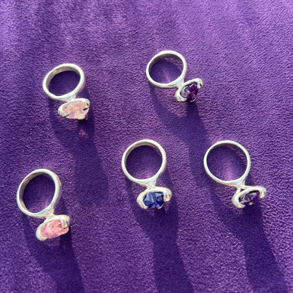 Five silver rings with gemstones on a purple fabric background